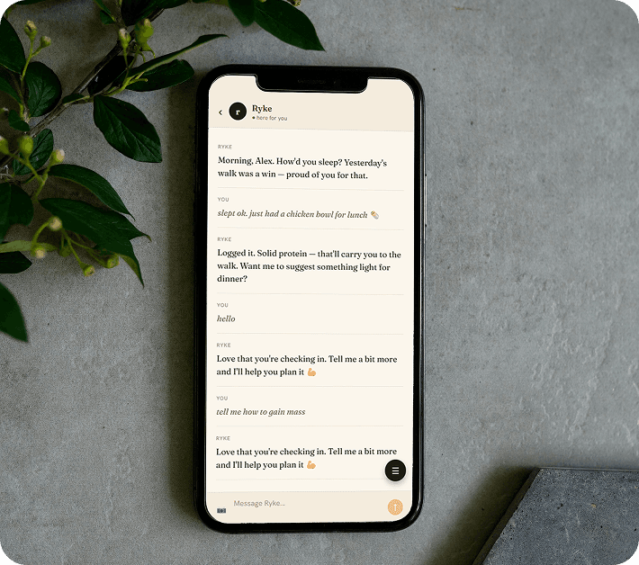 A phone on a table showing a Ryke text thread — a morning check-in, a chicken bowl logged from a message, and an offer to suggest a lighter dinner